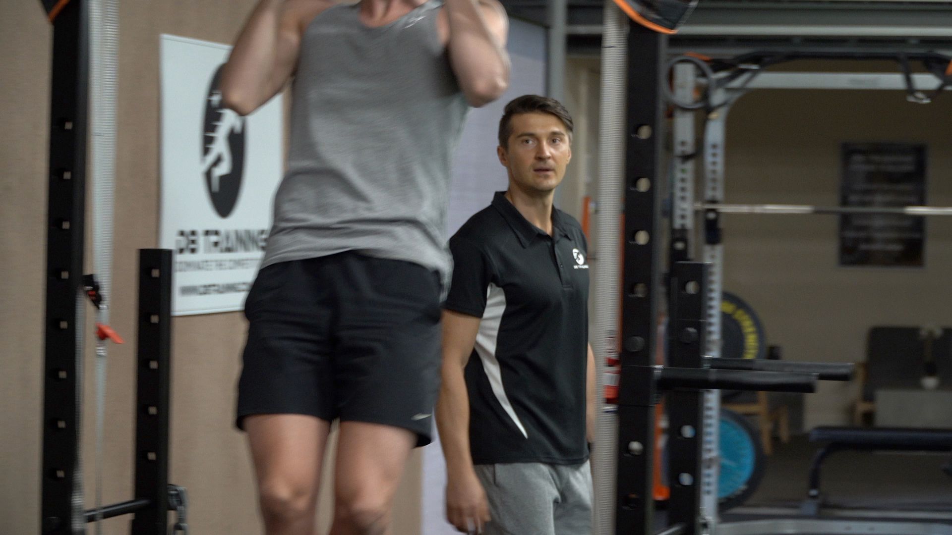 Man doing pull-ups in a gym while a trainer watches nearby