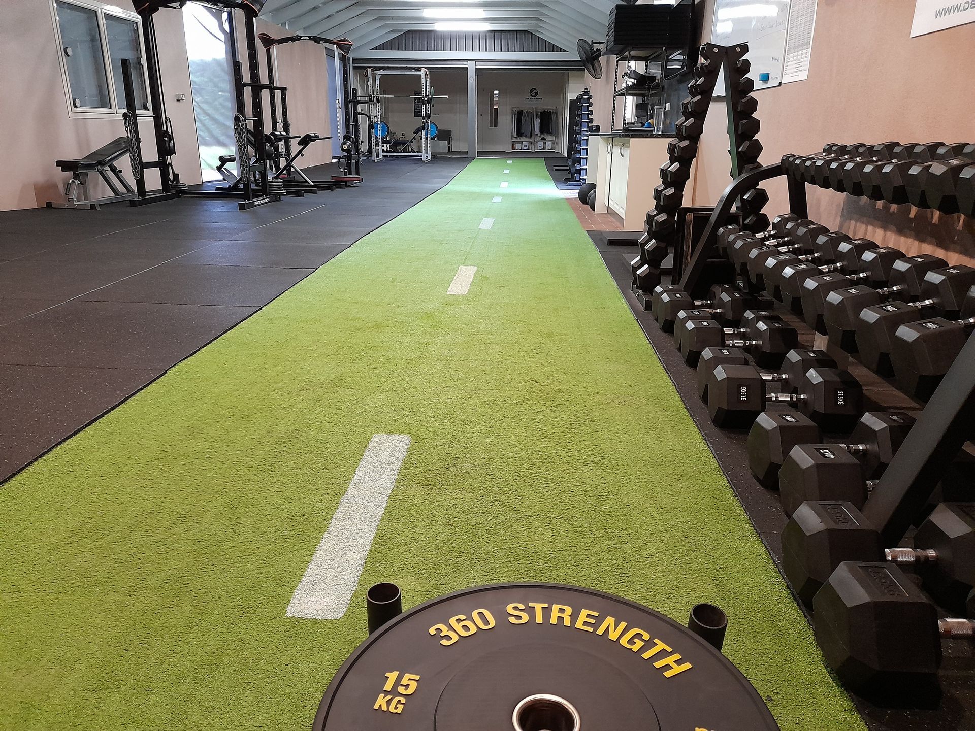 Gym with green turf lane, dumbbells, and equipment in a mirrored workout room.