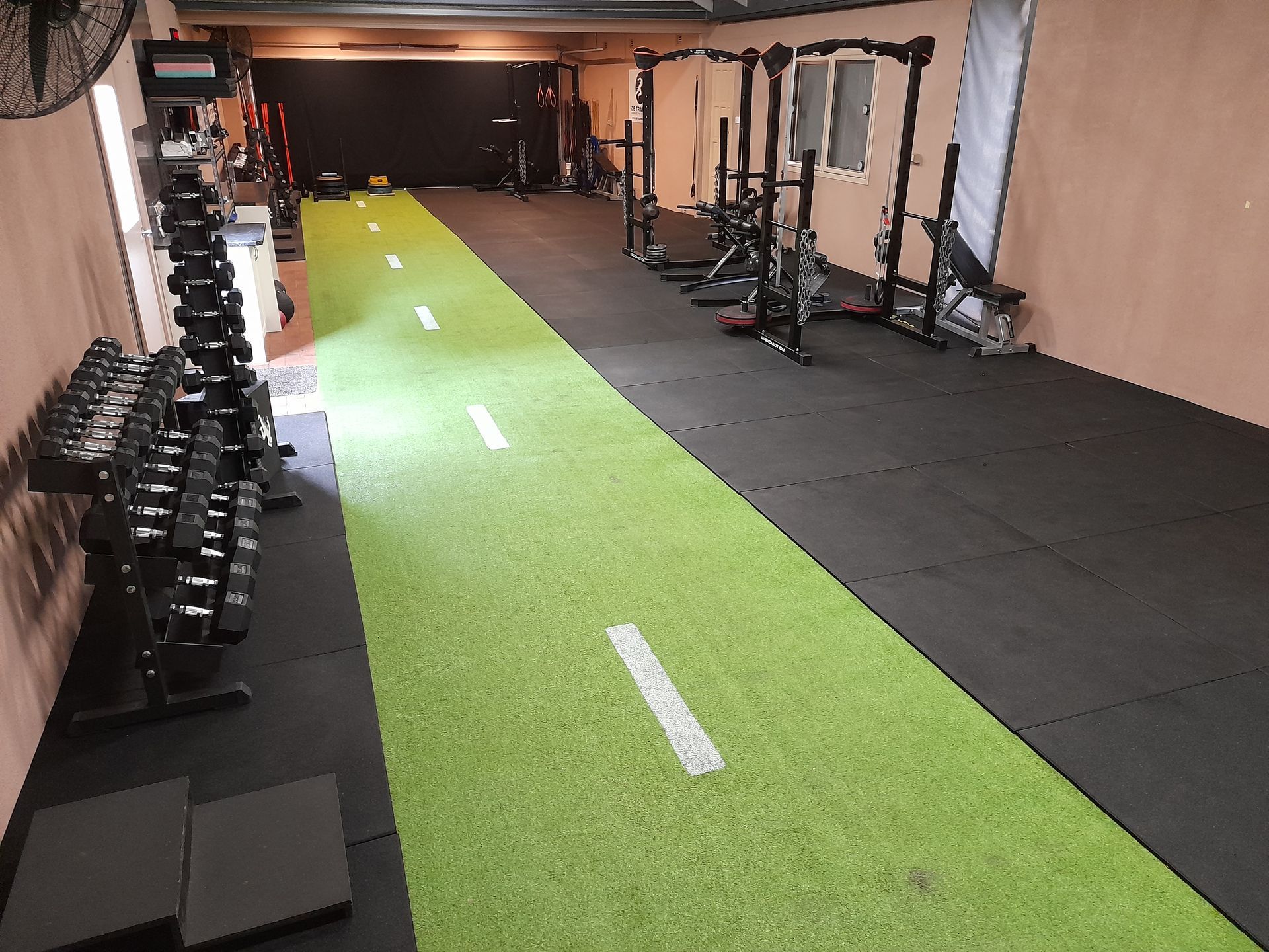 Indoor gym with green turf strip, dumbbells, and squat racks along the walls