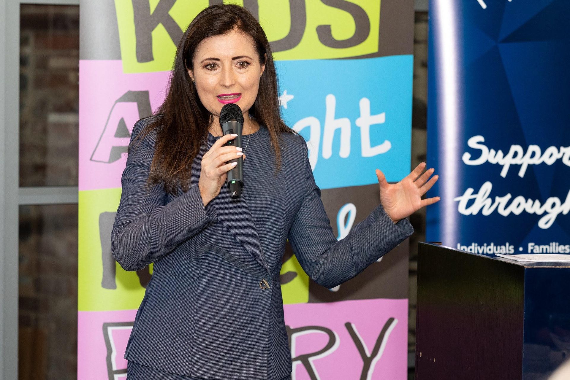 A woman is standing in front of a sign holding a microphone.