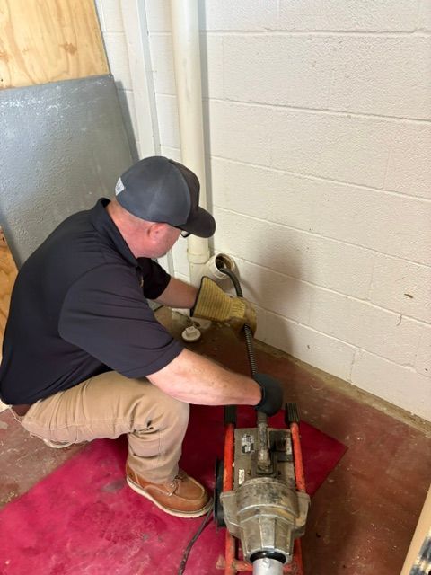 Worker operating a red floor-grinding machine against a wall in a small room