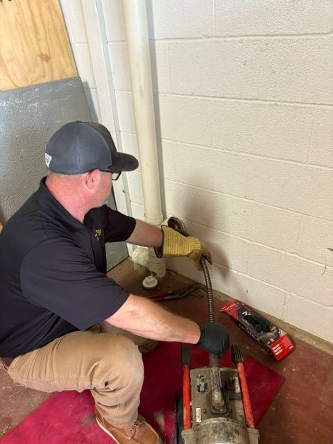Worker using a hand tool to repair plumbing beside a basement wall and exposed pipes