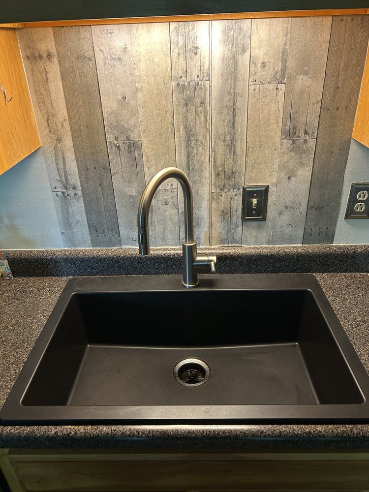 Kitchen sink with black countertop, chrome faucet, and gray wood backsplash panels