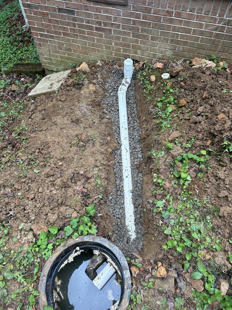Backyard trench with white drain pipe running to a brick wall, and an open utility box in the foreground