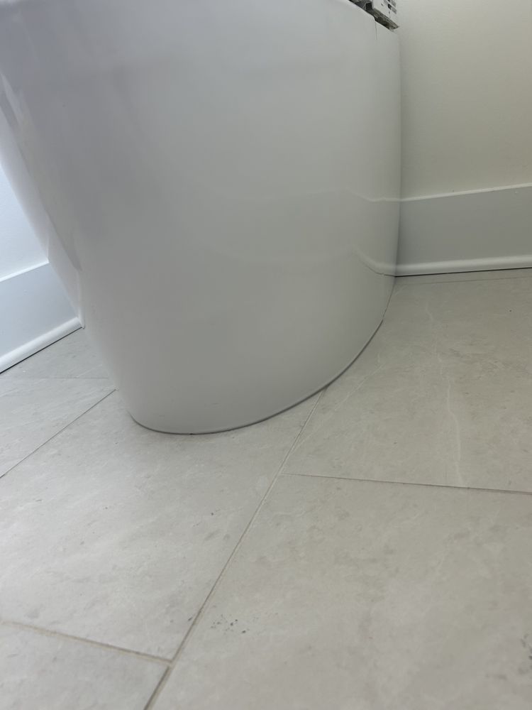 White toilet base on a light gray tiled bathroom floor near a wall.
