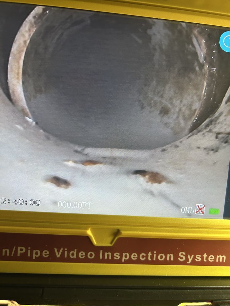 Cylindrical pipe interior shown on a pipe inspection monitor, with dirt and corrosion visible near the bottom.