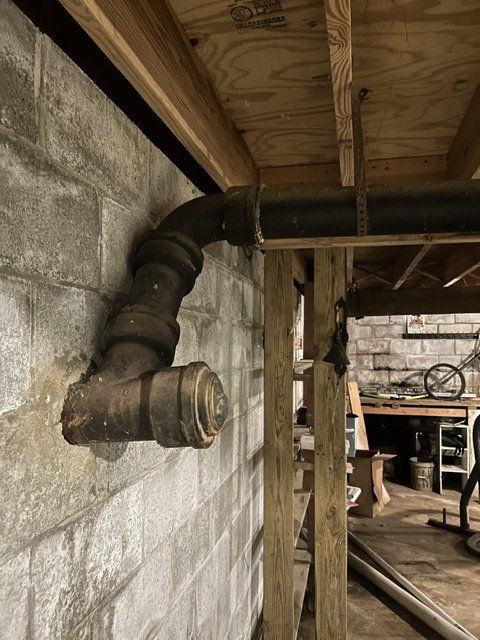 Basement crawlspace with exposed duct and pipe through a cinder block wall under wooden beams.