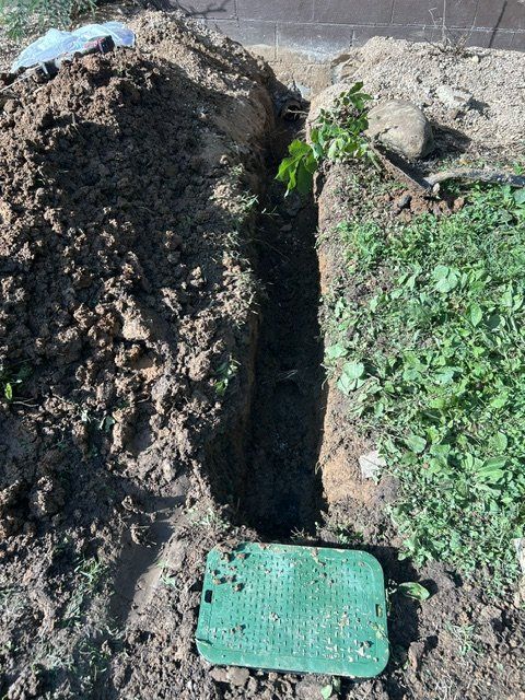 Narrow trench between dirt mounds with green vegetation and a teal grate at the bottom