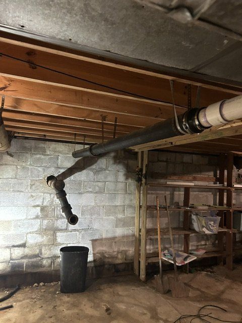Basement with exposed pipes, cinder block wall, shelves, and a trash can on the floor