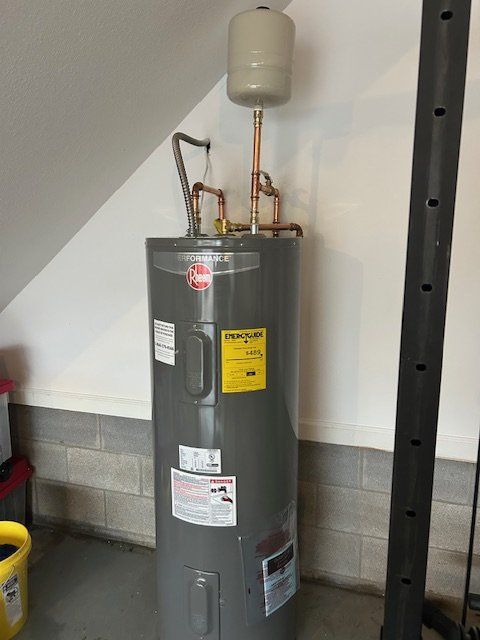 Water heater with pipes and expansion tank in a basement utility area, beside a metal support post.
