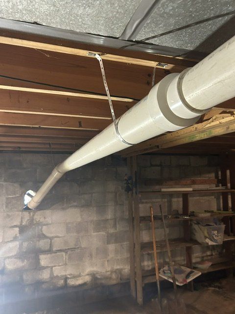 White PVC pipe runs across basement ceiling toward a cinder block wall and metal shelving.