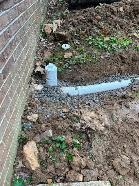 Brick wall beside a muddy excavation with white PVC pipe and a small plastic bottle
