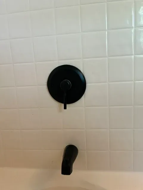 White tiled shower wall with black faucet and round control handle