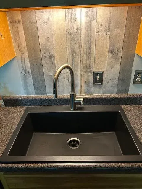 Kitchen sink with black basin, stainless faucet, and gray wood backsplash above dark countertop