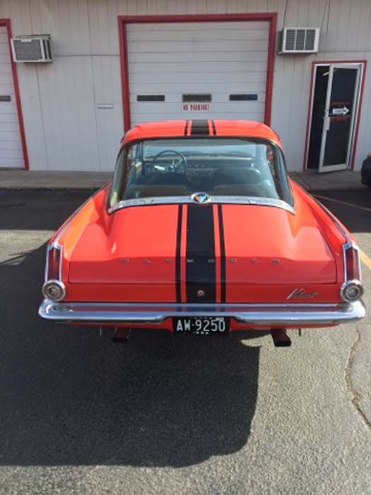 Red vintage car with black racing stripes parked in front of a garage.