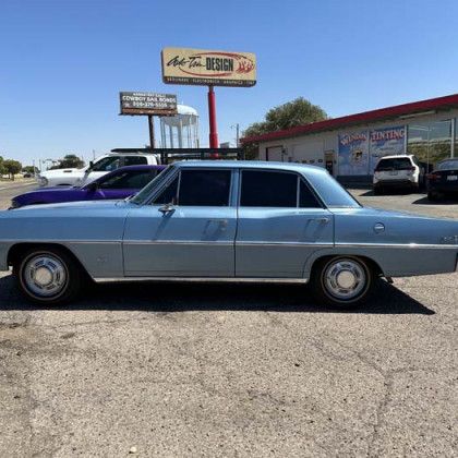 Light blue classic car parked in front of a shop, sunny day.