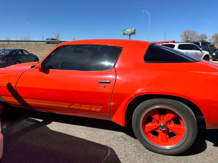 Orange 1970s Chevrolet Camaro with tinted windows and red wheels parked outdoors on a sunny day.