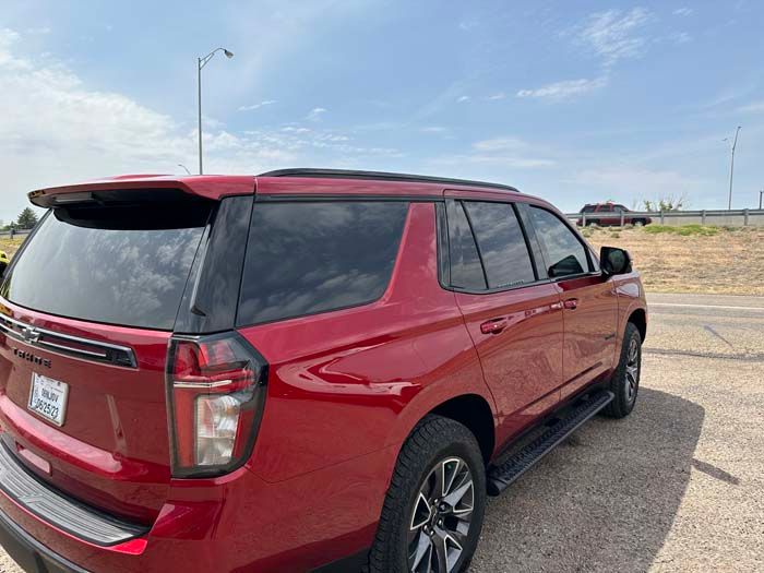 Red Chevrolet Tahoe SUV parked on the side of a road under a partly cloudy sky.