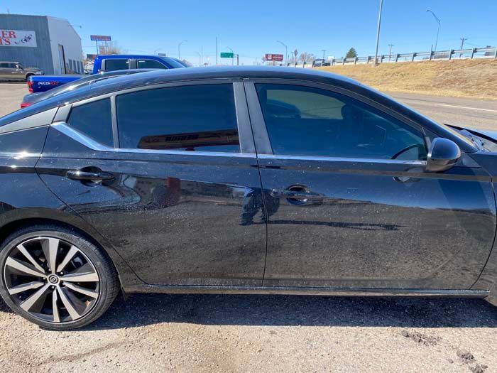 Black sedan with tinted windows, parked on pavement near a road.