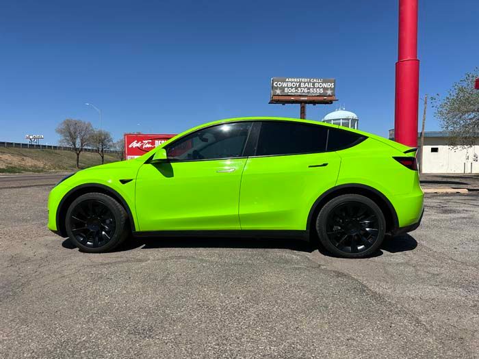 Lime green Tesla Model Y with black rims parked outdoors under a blue sky.