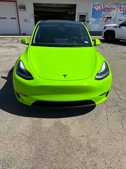 Bright green Tesla Y in front of a business with a window tint sign.
