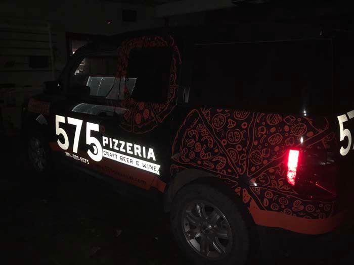 Black delivery truck with reflective graphics for 575 Pizzeria, parked at night.