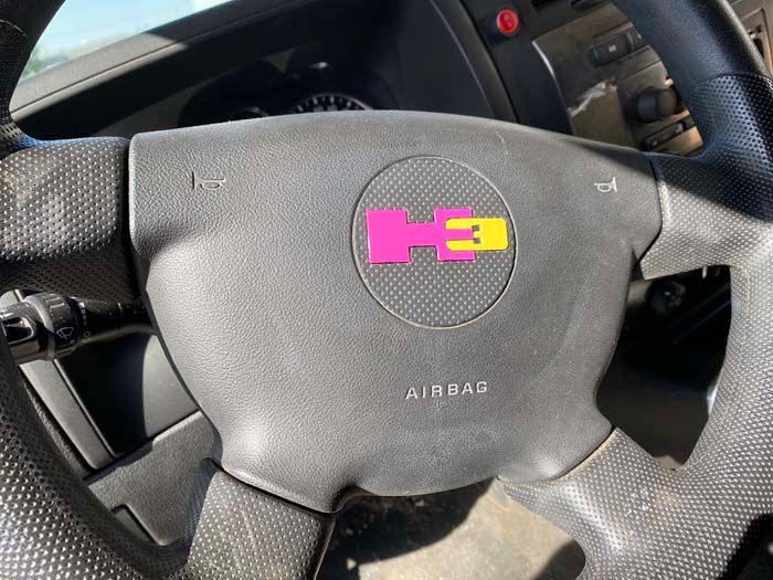 Black steering wheel with a pink and yellow Hummer logo in the center.