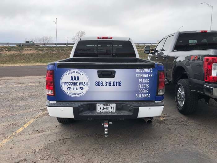 Rear of a white pickup truck with blue advertisement for AAA Pressure Wash, and the phone number 806.318.0118. Parked beside another pickup.