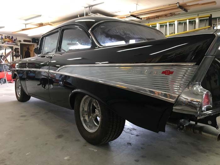 Black 1957 Chevrolet Bel Air coupe in a garage, with shiny chrome accents.