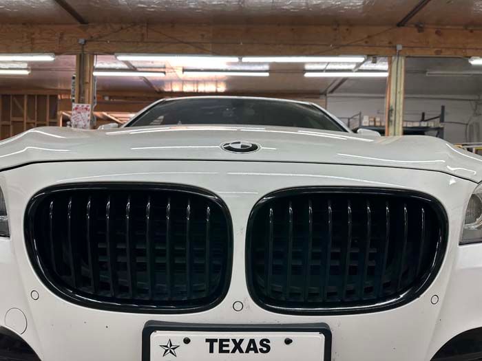 White BMW car with black grill, Texas license plate, in a garage.