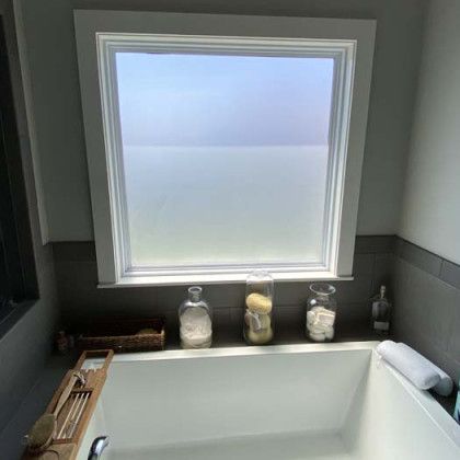 A bathroom with a frosted window above a bathtub with toiletries on a shelf.