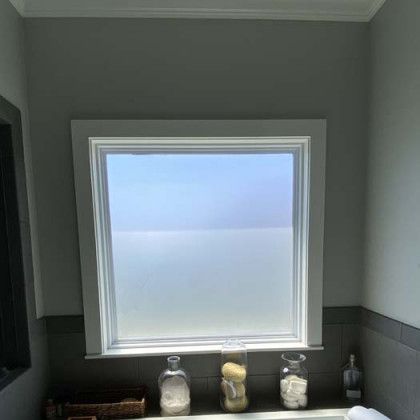 Window in a bathroom with frosted glass, below window are jars and a small shelf.