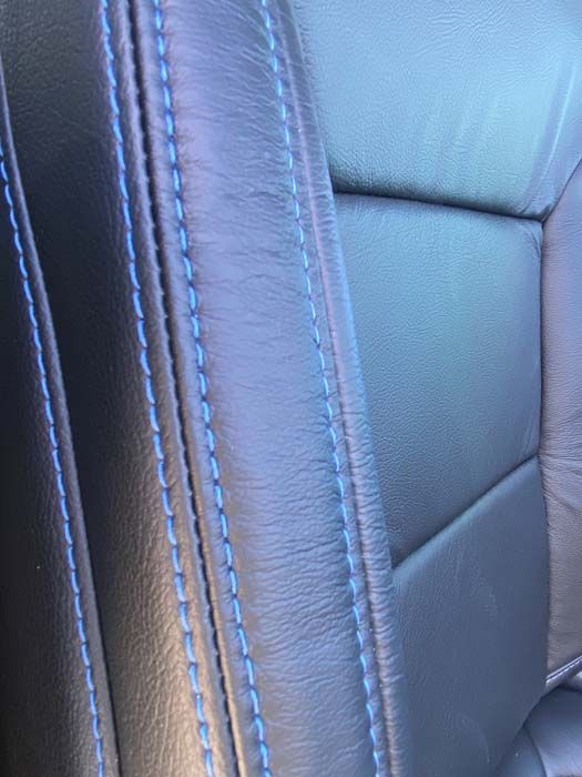 Black leather car seat with blue stitching detail.