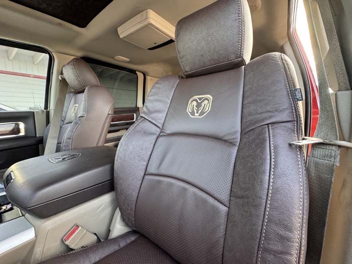 Brown leather interior of a Ram truck, with a headrest featuring the Ram logo and a center console.
