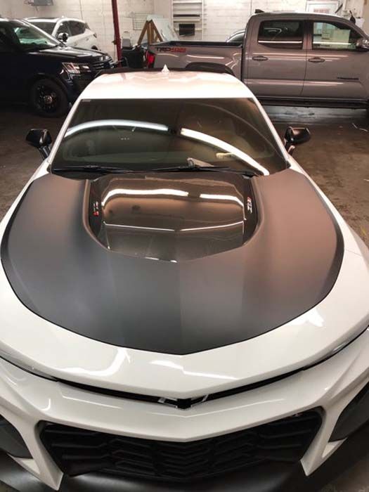 White sports car with a matte black hood in a garage.