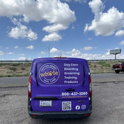 Purple Central Bark Dog Care van with services listed, parked on a road under a cloudy blue sky.