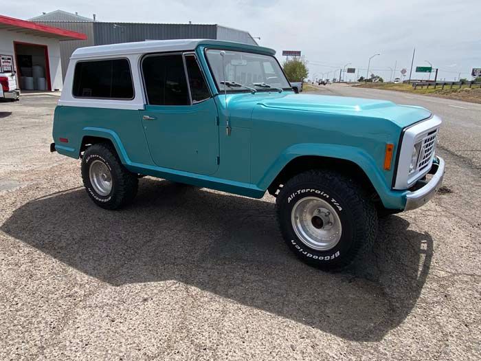 Teal and white vintage Jeepster Commando parked on asphalt in front of a building.