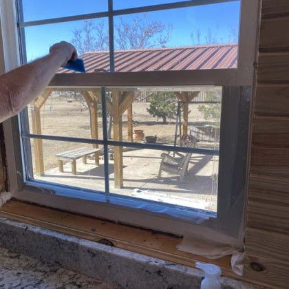 Person using a squeegee to apply film to a window, a gazebo and outside view visible through the window.