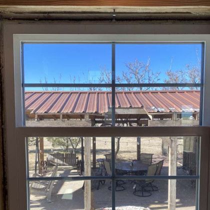 View through a window of a backyard scene; tables and chairs in the foreground, and a building with a red roof in the background.