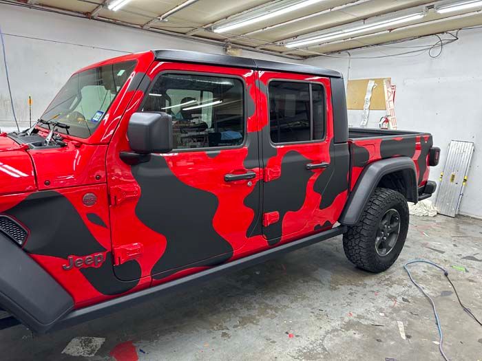 Red Jeep Gladiator pickup truck with black camouflage wrap.