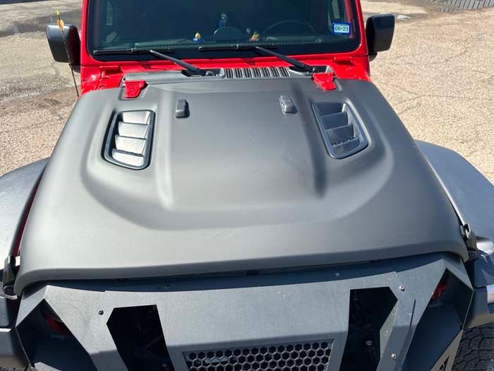 Red Jeep with gray hood featuring vents, parked outdoors.