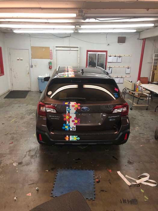 Brown Subaru Outback with colorful flower decals in a workshop.