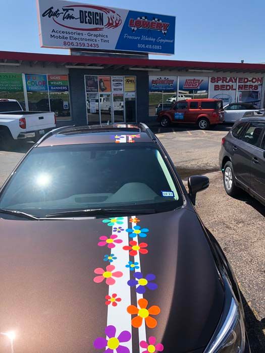 Brown car decorated with flower stickers in front of an auto shop with a sign.