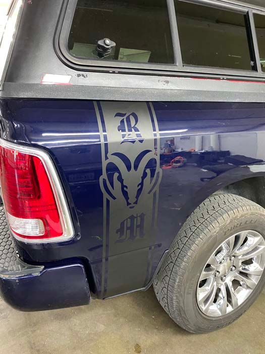 Blue truck bed with black Ram logo stripe, silver wheel, and red tail light.
