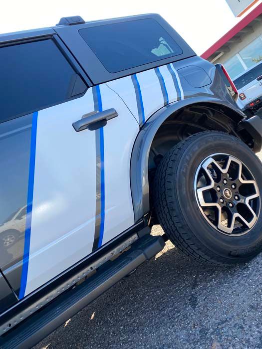 White Ford Bronco with blue and black stripes on the side, parked outside.