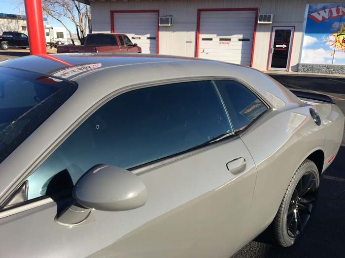 Gray Dodge Challenger parked in front of a building with window tinting services.