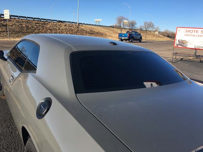 A light-colored Dodge Challenger with tinted rear windows is parked outside on a sunny day.