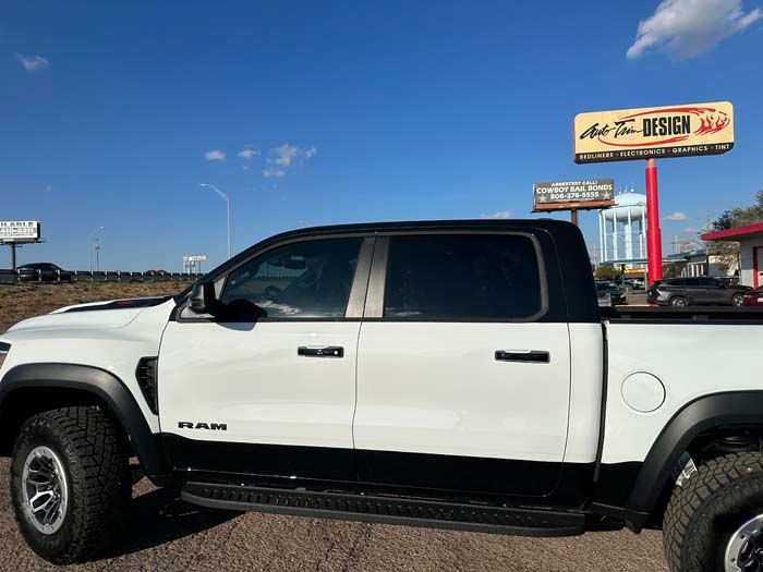 White and black Ram TRX truck parked near a sign on a sunny day.