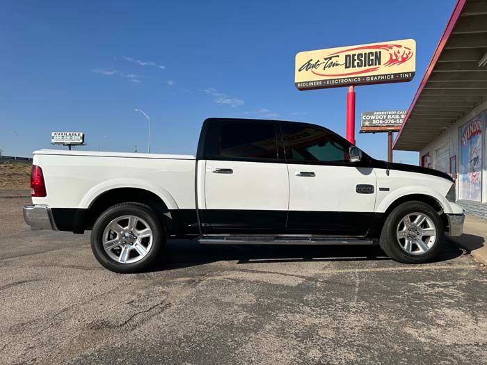 Two-tone white and black Dodge Ram pickup truck parked outside a business with sign that says 