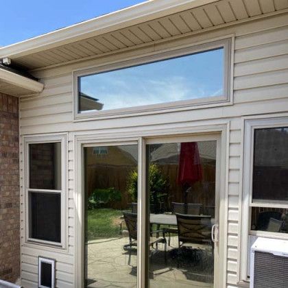 Exterior view of a house with sliding glass doors, windows, and a large window above. Sky and a backyard are visible.